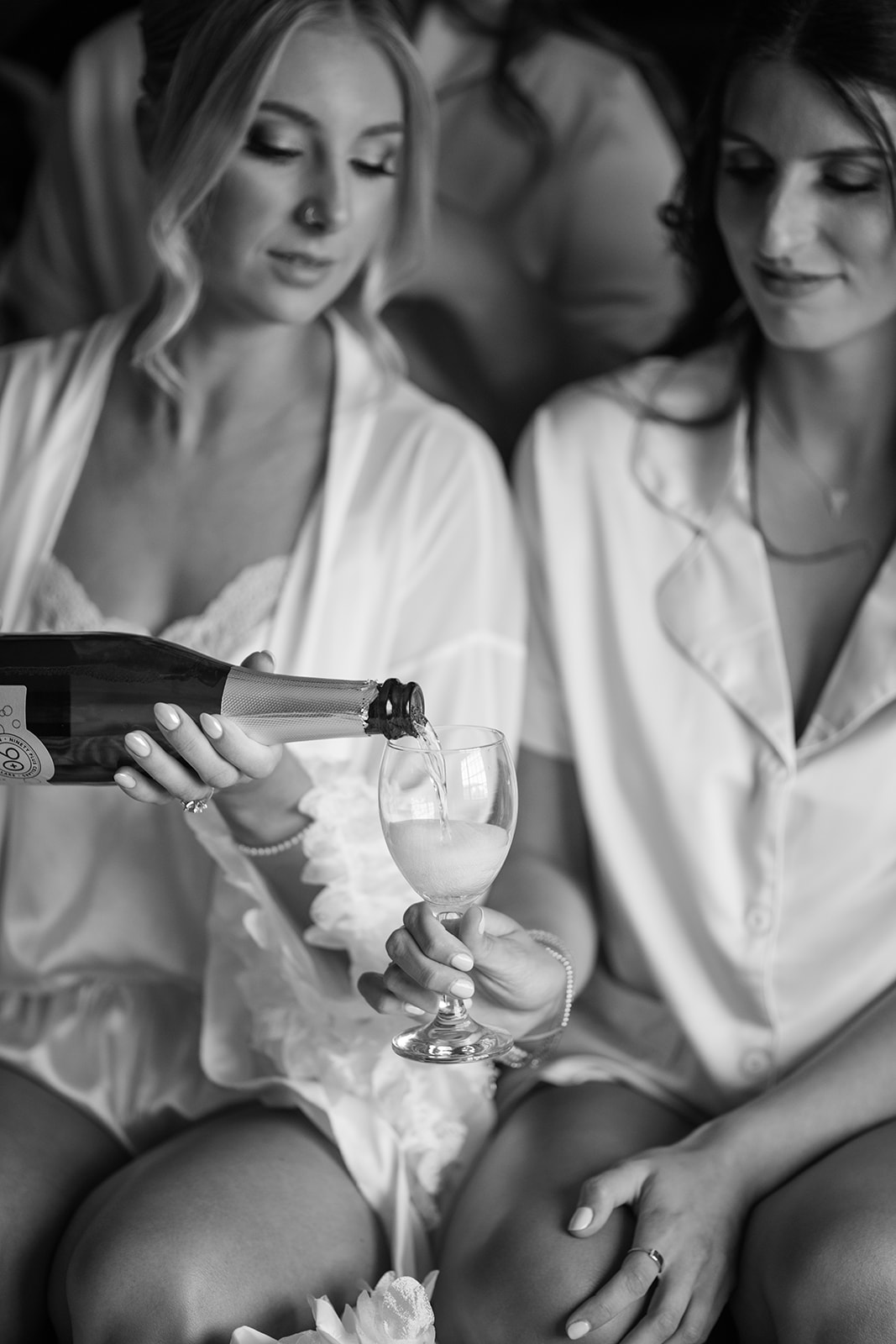 Black and white photo of the bride pouring bubbly champagne into her bridesmaid's glass during prep.